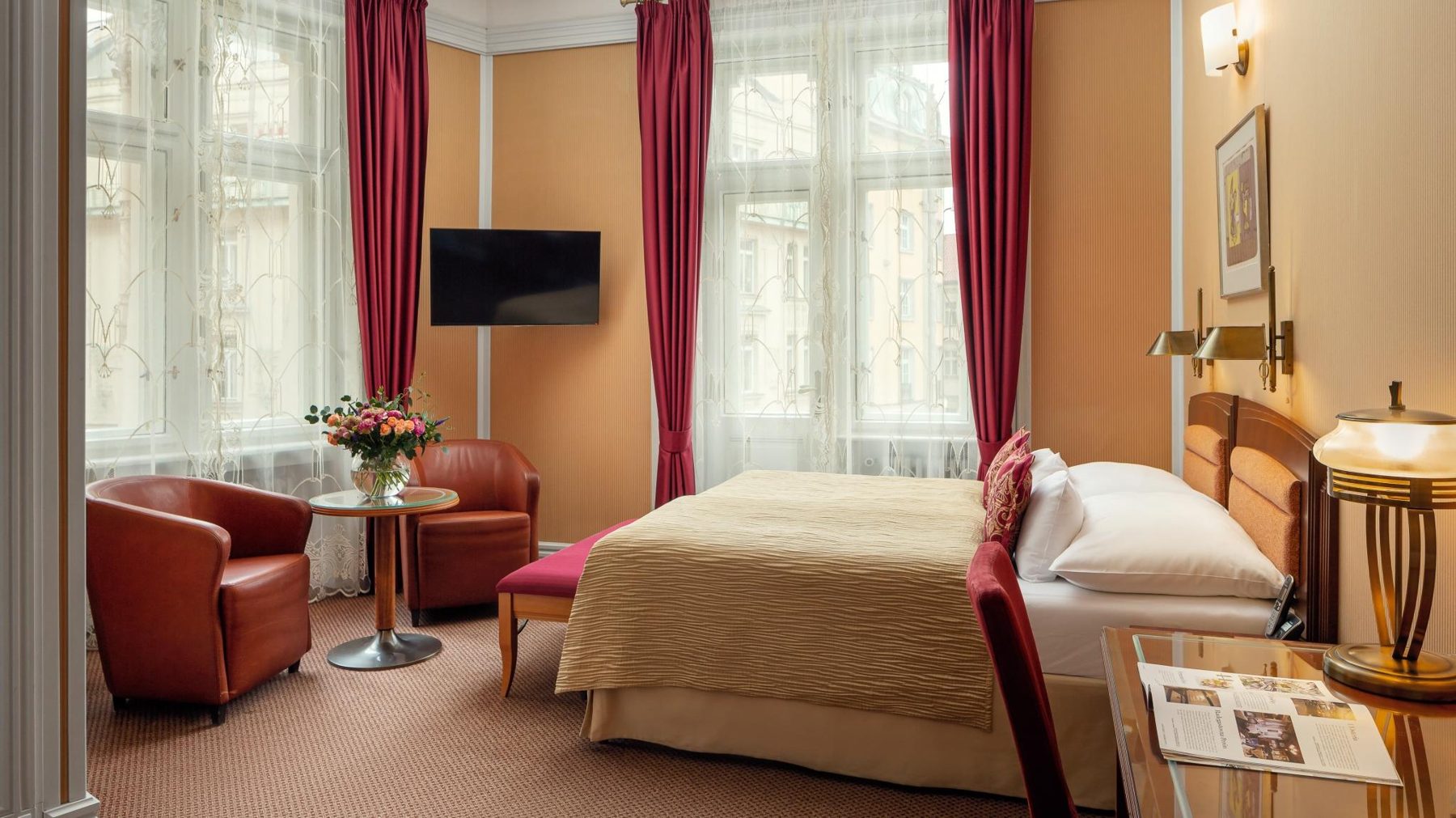 Executive bedroom with a double bed, red curtains and two chairs by the windows.
