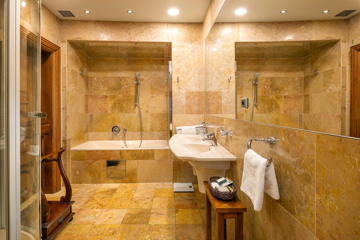 Marble-lined bathroom with a bath, basin and large wall mirror.