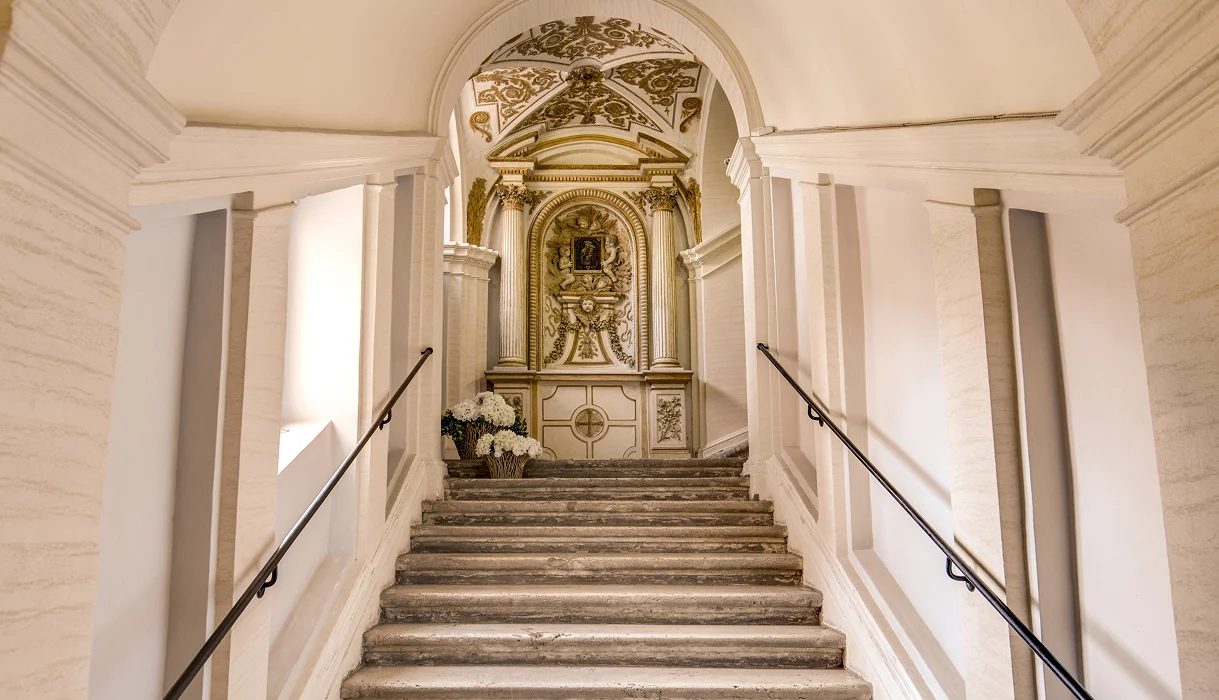 Stone staircase with handrails leading towards an ornate niche beneath a decorated arch.