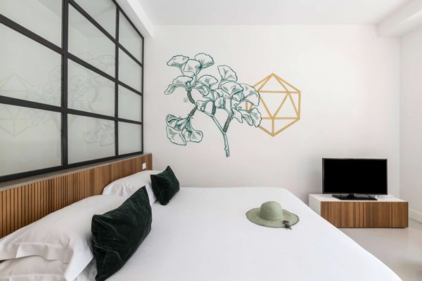 White bed beneath botanical line art and a black-framed partition.