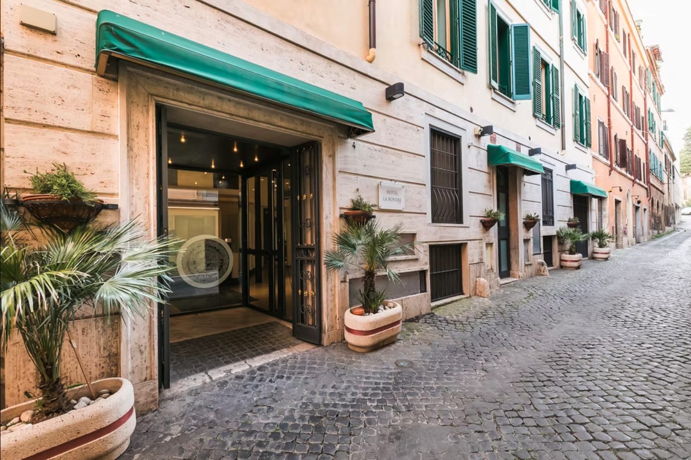 Hotel La Rovere entrance with green awnings and potted plants beside a cobbled lane.