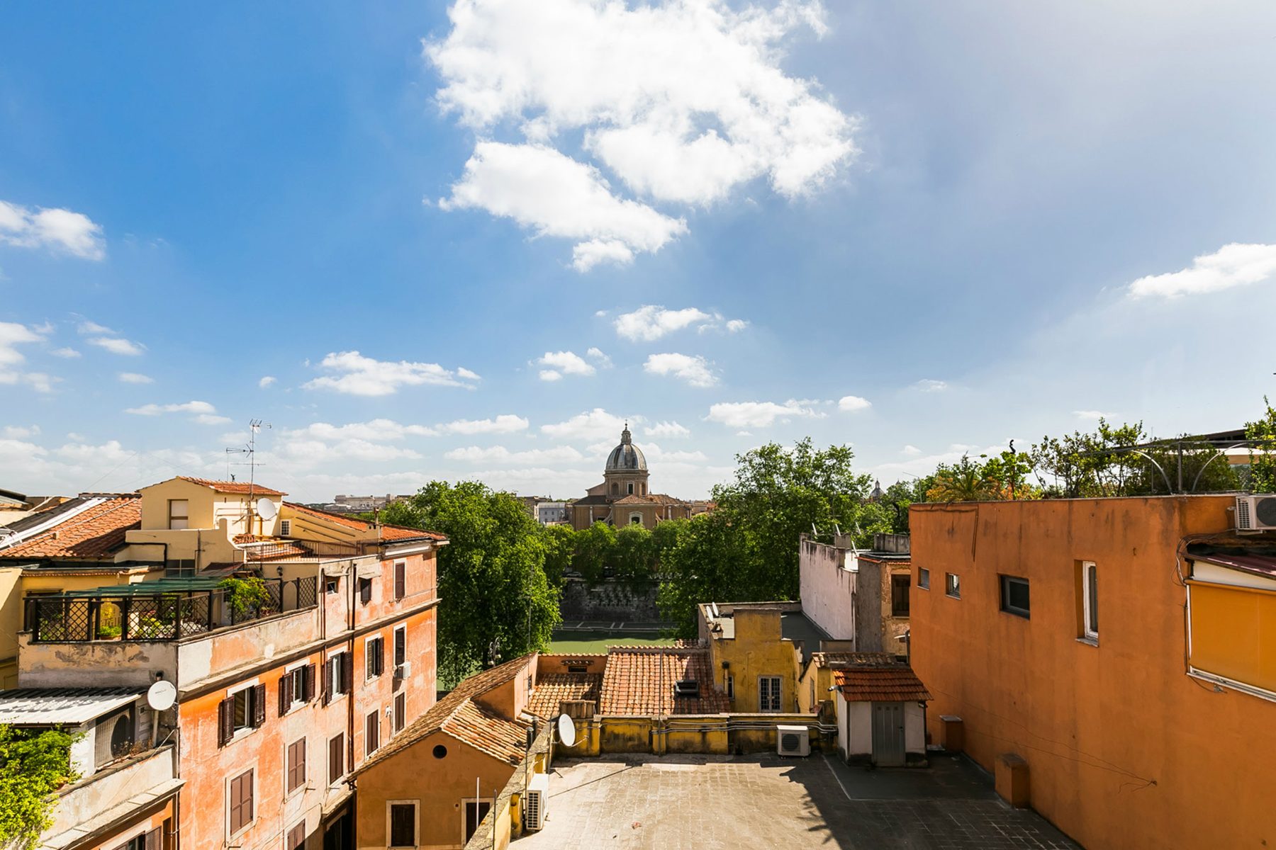 Terracotta buildings, trees and a domed church beneath a blue sky.