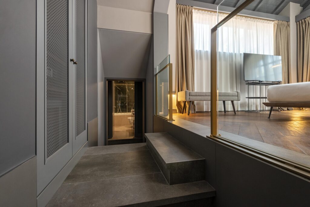 Short dark staircase beside a glass partition leading into a bedroom.