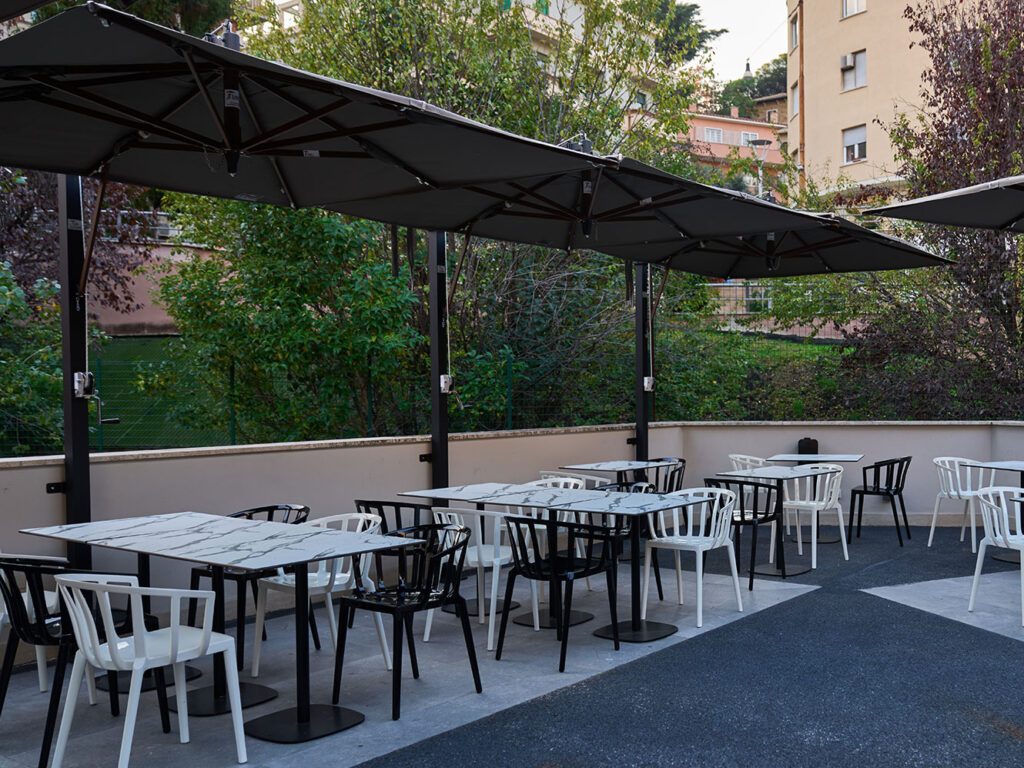 Black and white chairs around tables beneath dark parasols on a planted terrace.