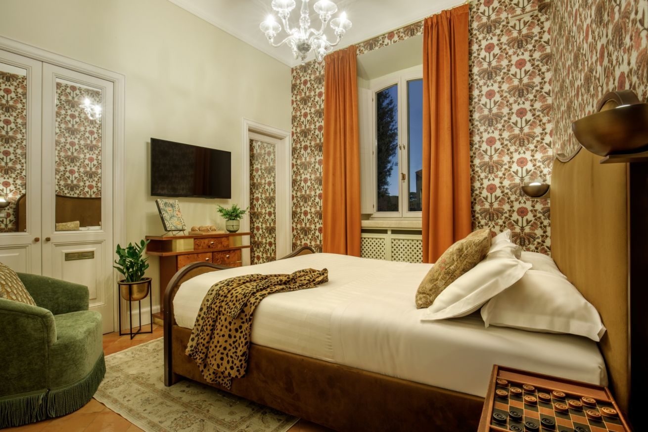 Bedroom with patterned wallpaper, curved bed frame, orange curtains and green chair.
