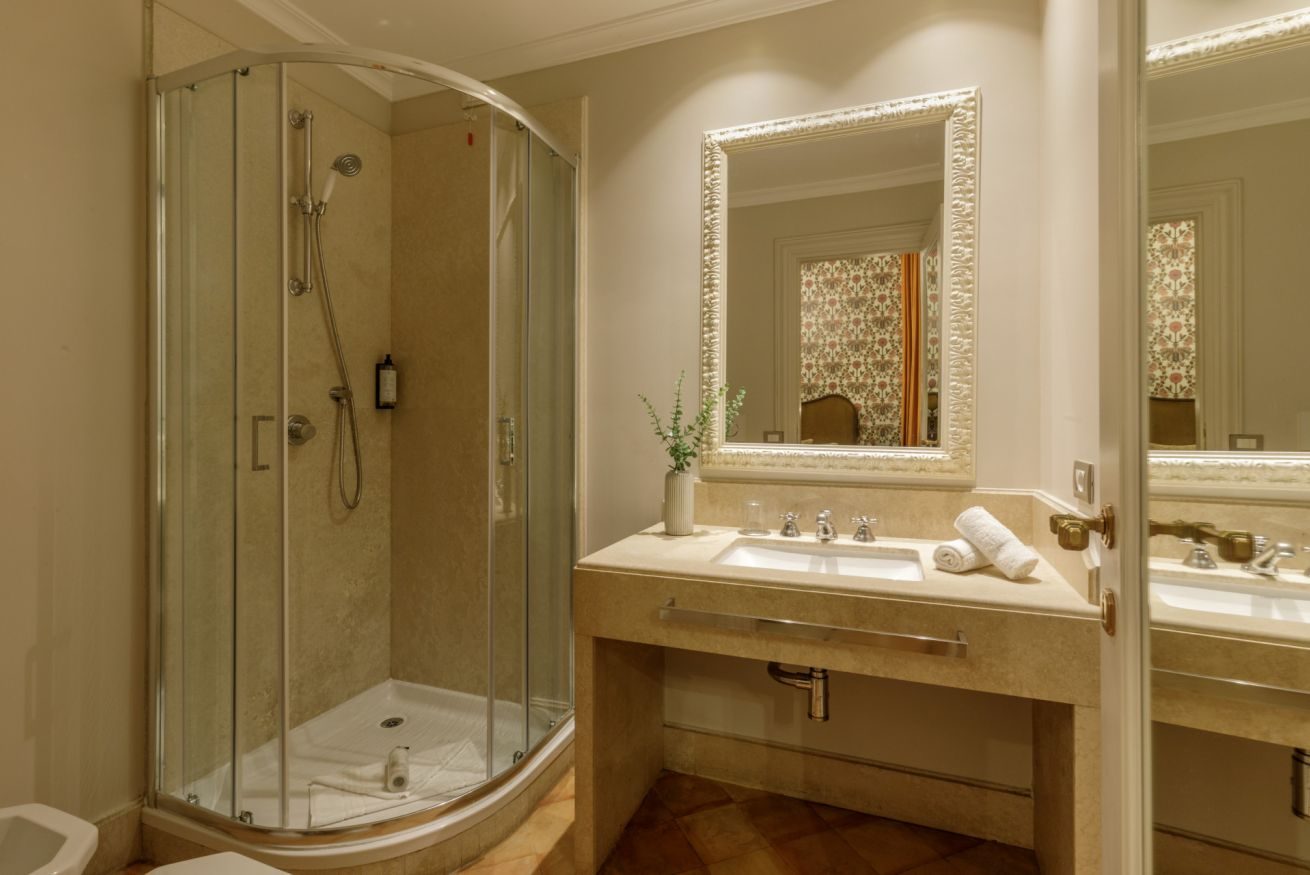 Curved glass shower beside a basin and large framed mirror.