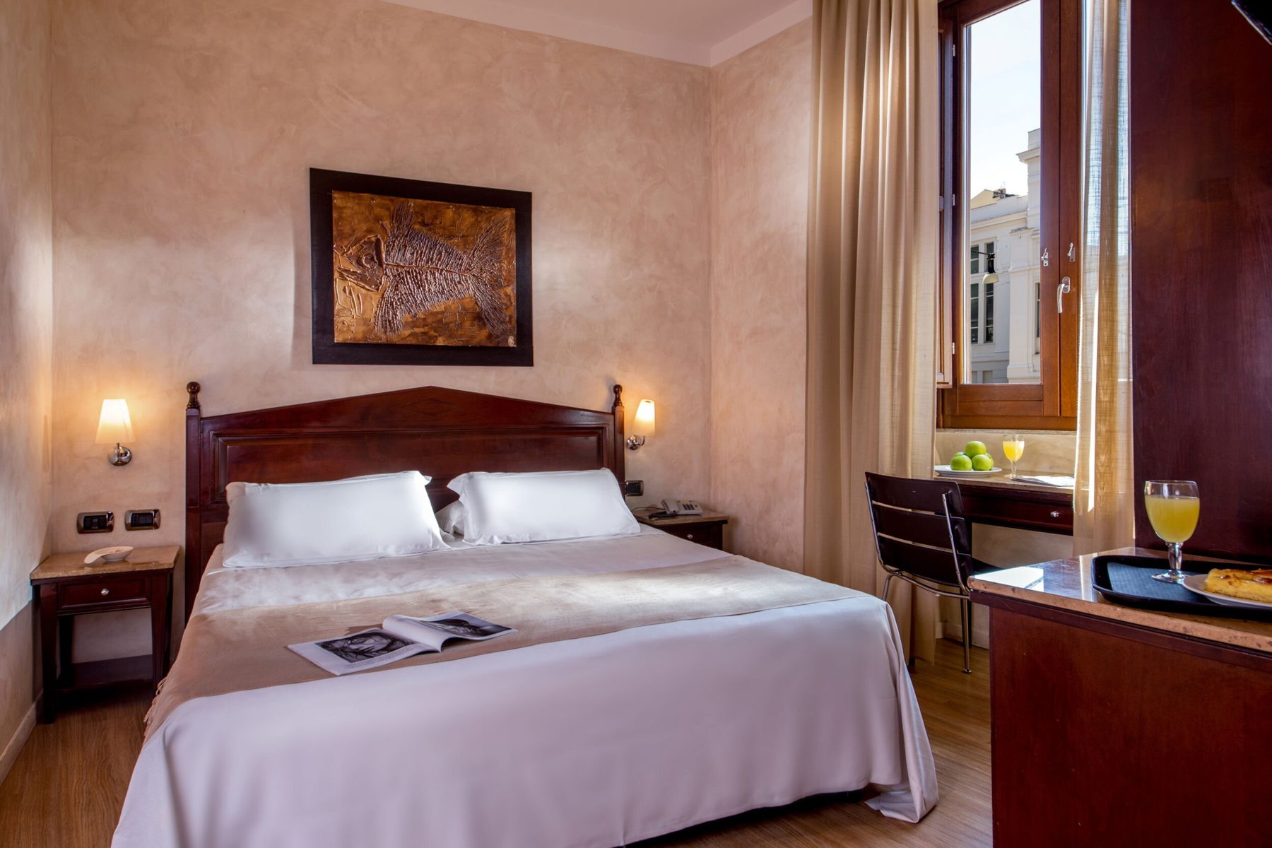 Double bedroom with wooden headboard, bedside lamps and a window beside the desk.