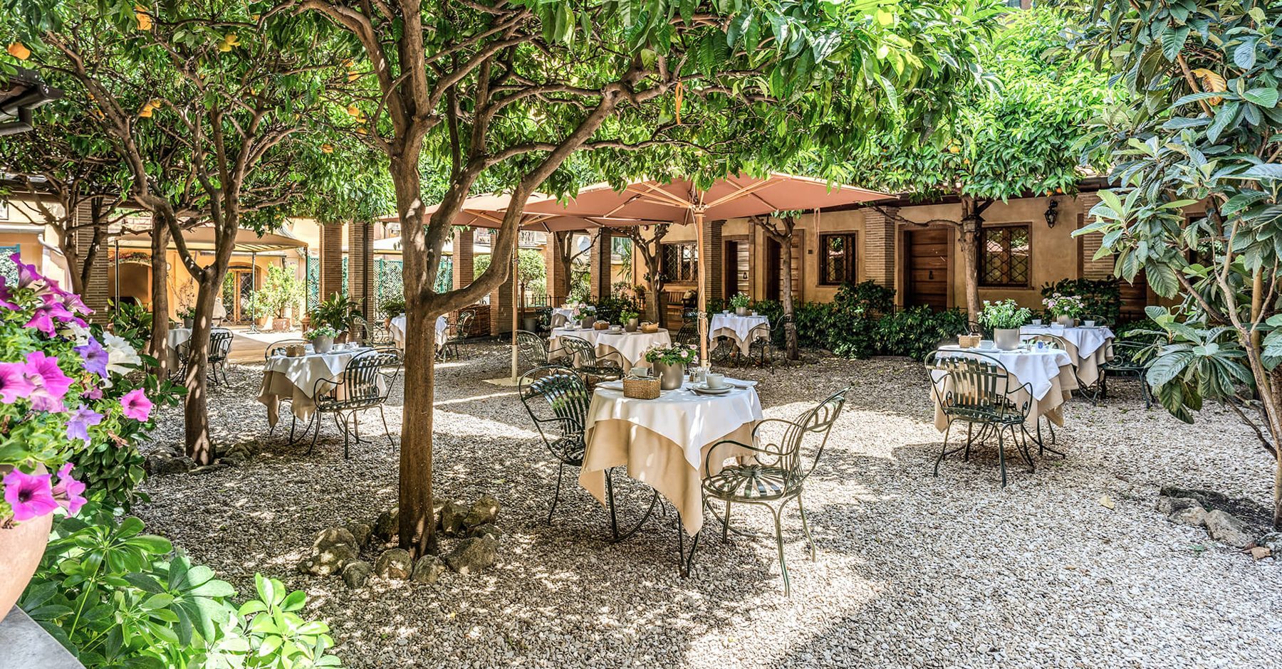 Tables beneath trees and parasols in the hotel courtyard.