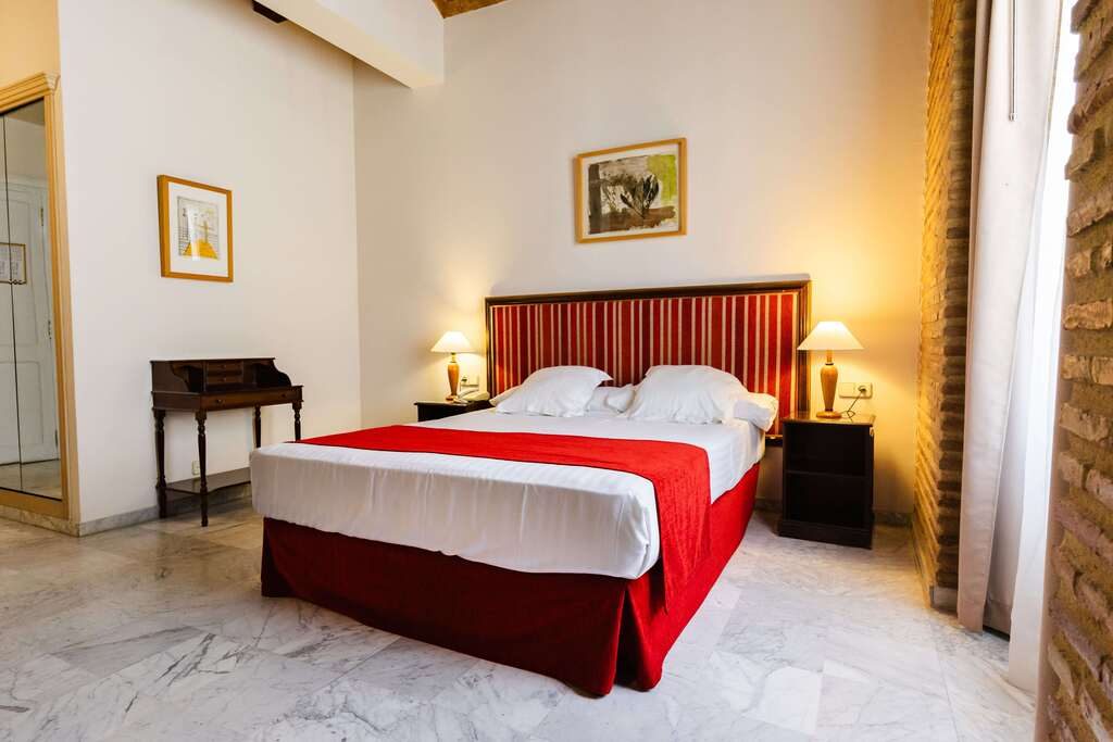 Bed with a red runner, tall windows, pale floor and exposed stonework in an Ad Hoc Double Room.