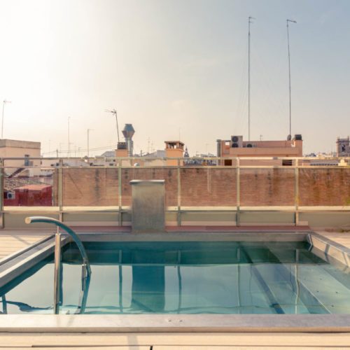 Compact rooftop pool with a metal ladder, glass screening and Valencia rooftops beyond.