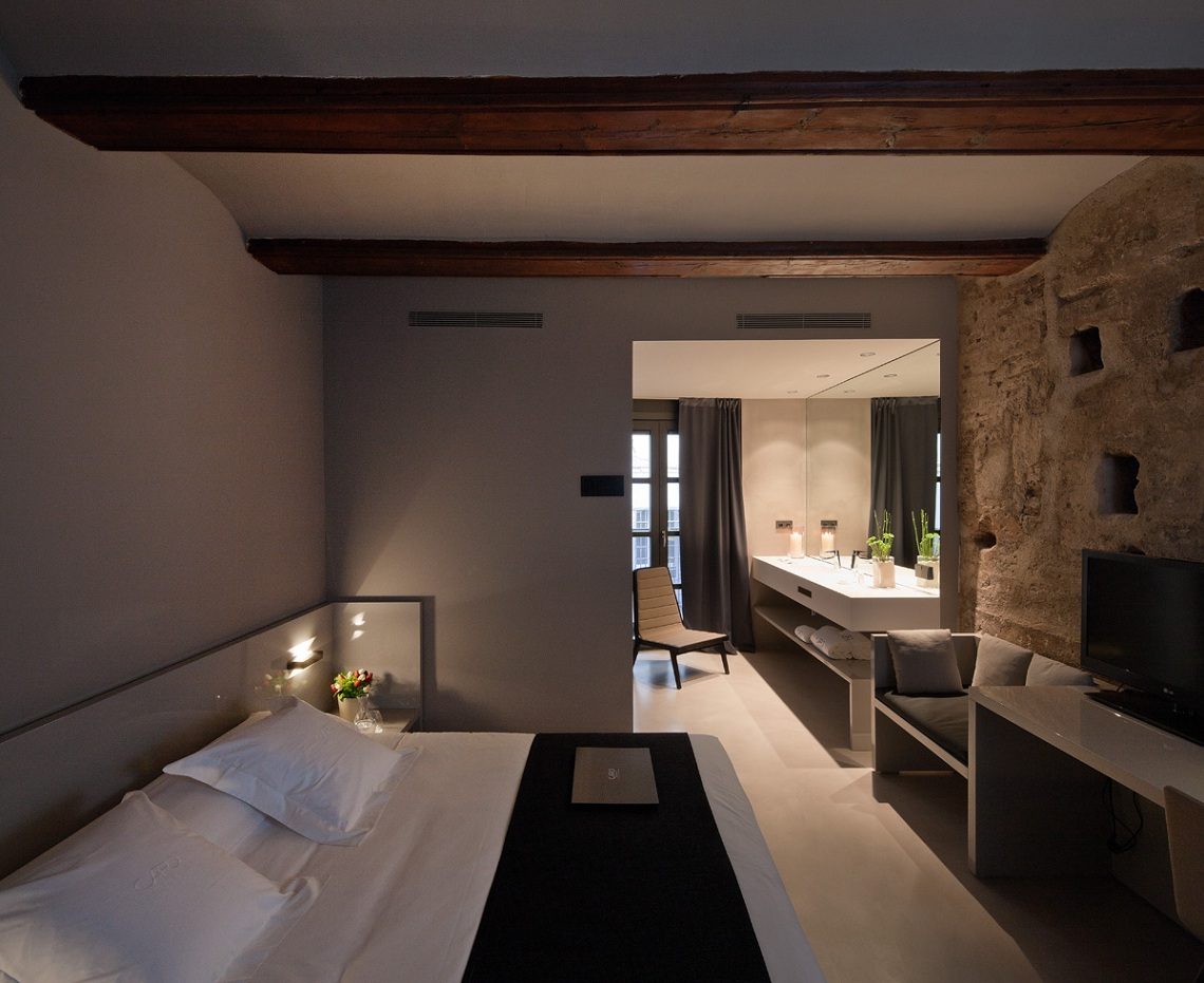 Double bed, exposed beams, masonry wall, desk and open vanity in a Caro Palace Double room.