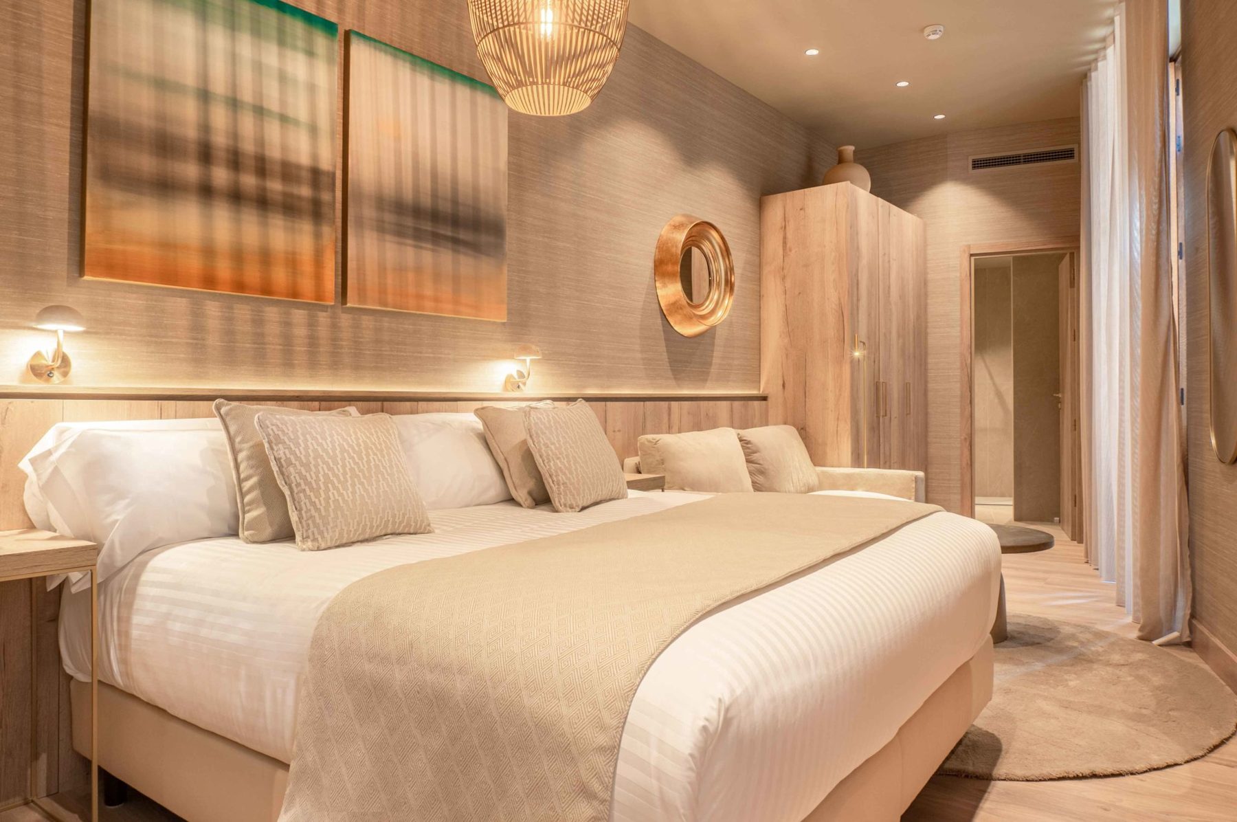 Bed, woven pendant, round gold mirror and timber wardrobe in a Corretgería Double Balcony room.