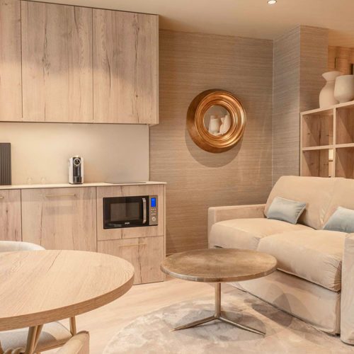 Timber kitchenette with a microwave, round tables and a sofa in Corretgería’s hotel gallery.