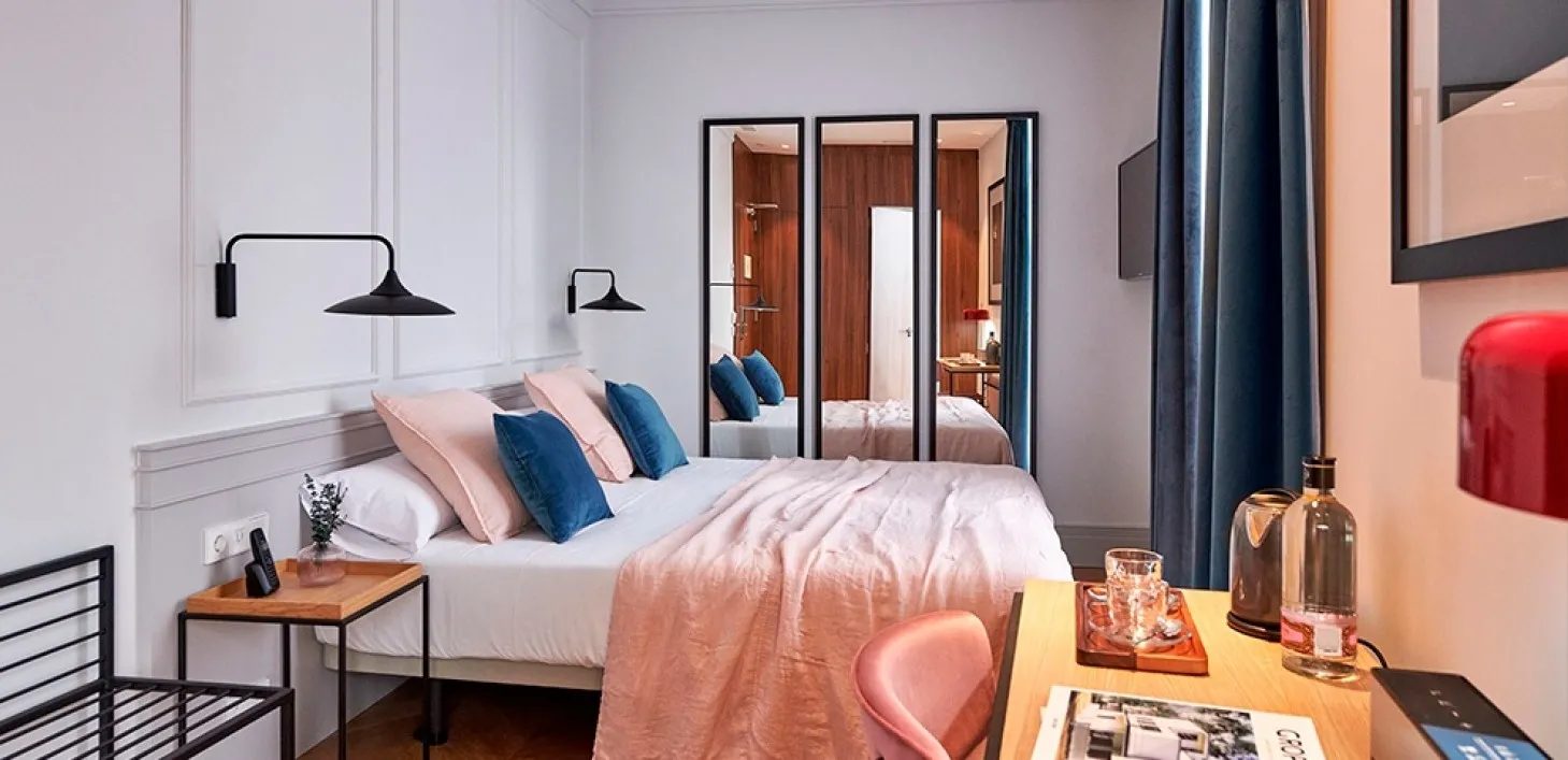 Bed with pink bedding, blue cushions, a desk and mirrors in Helen Berger’s Superior Double category.