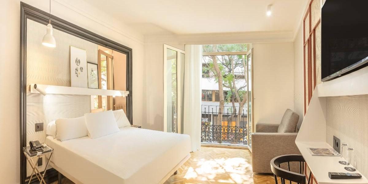 Bed, mirrored headboard, desk, armchair and open balcony doors in an SH Inglés Superior room.