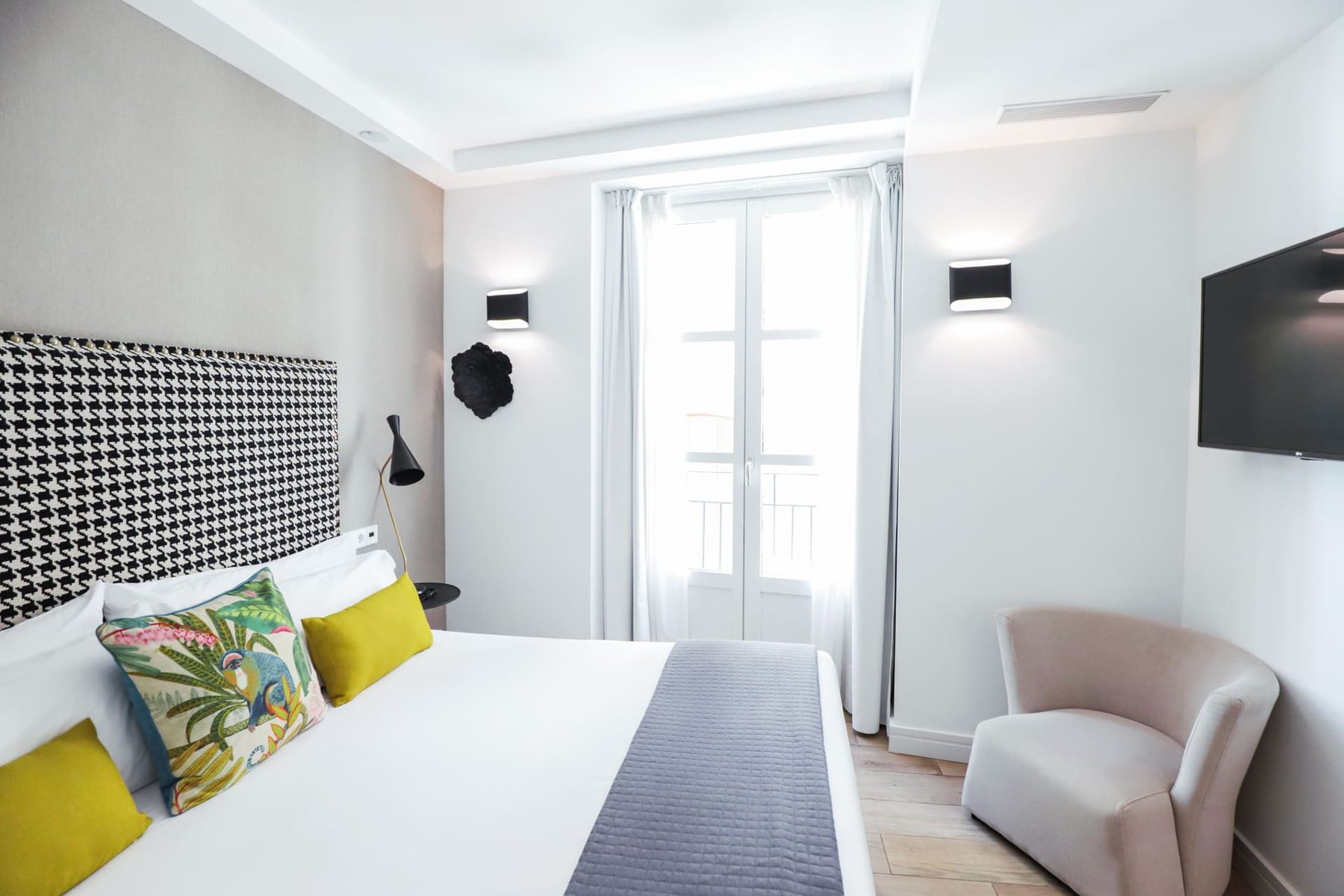 Bed with a patterned headboard, colourful cushions and tall balcony doors at Marqués House.
