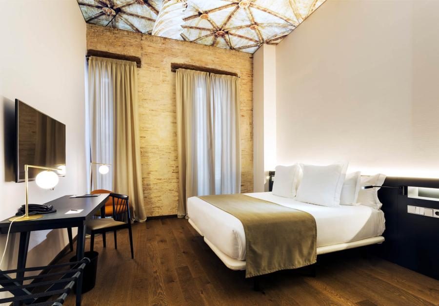 Bed, desk, tall curtains and a geometric illuminated ceiling in a One Shot Executive room.