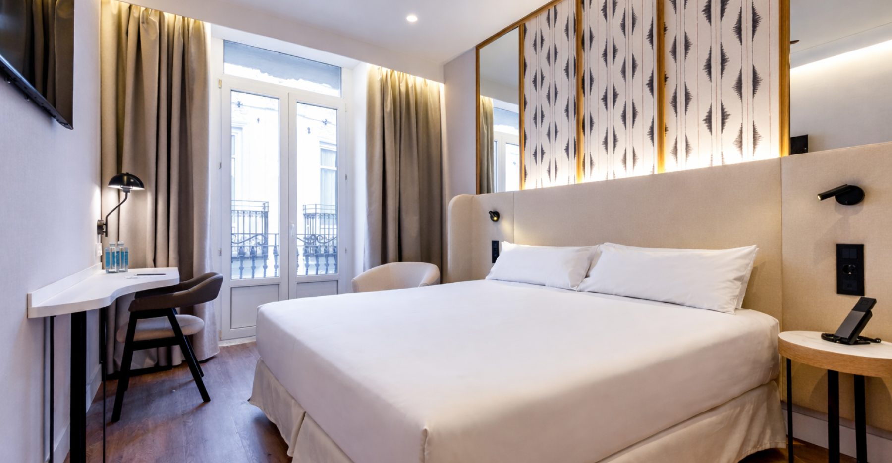Bed, desk and patterned wall panels beside tall balcony doors in a Petit Palace Double Room.