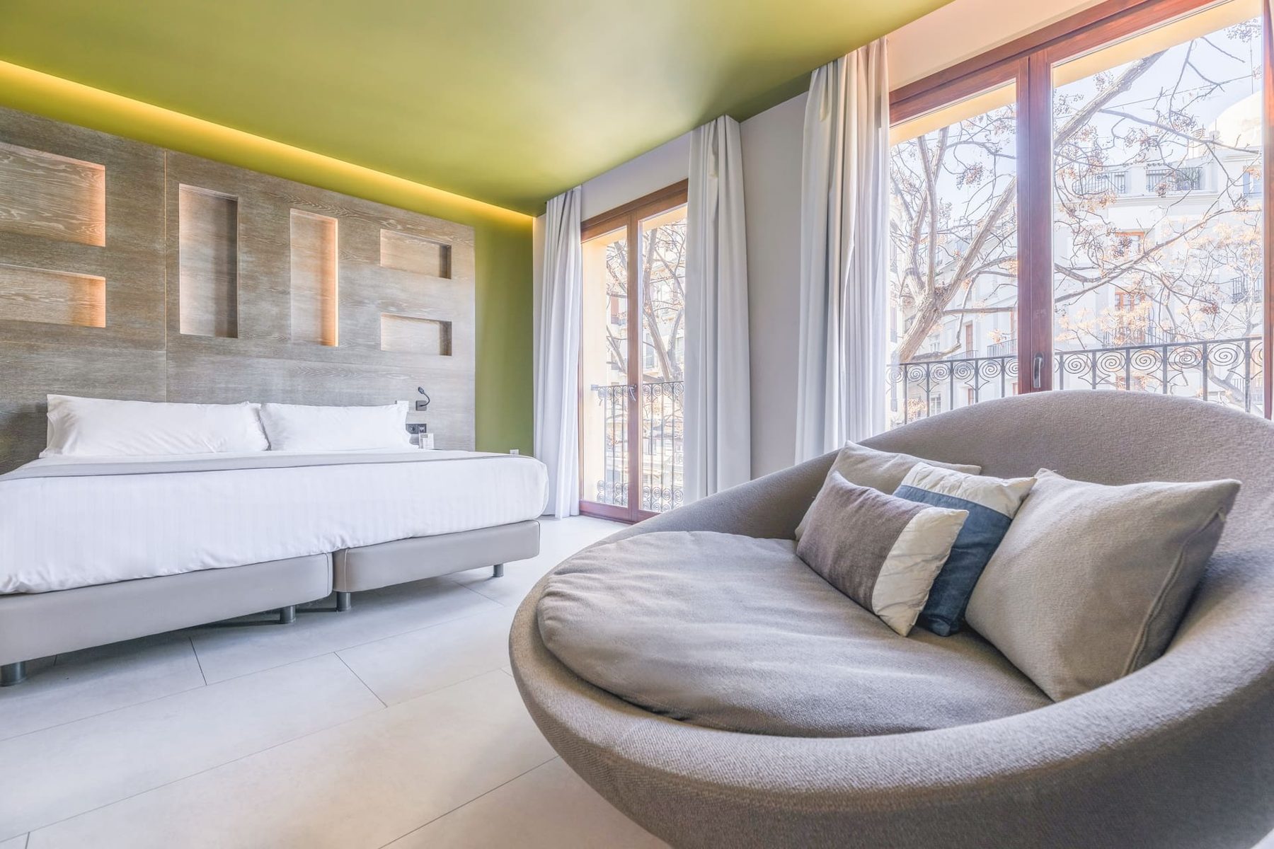 Bed, curved grey sofa and tall balcony windows in a Plaza Mercado Double Exterior room.