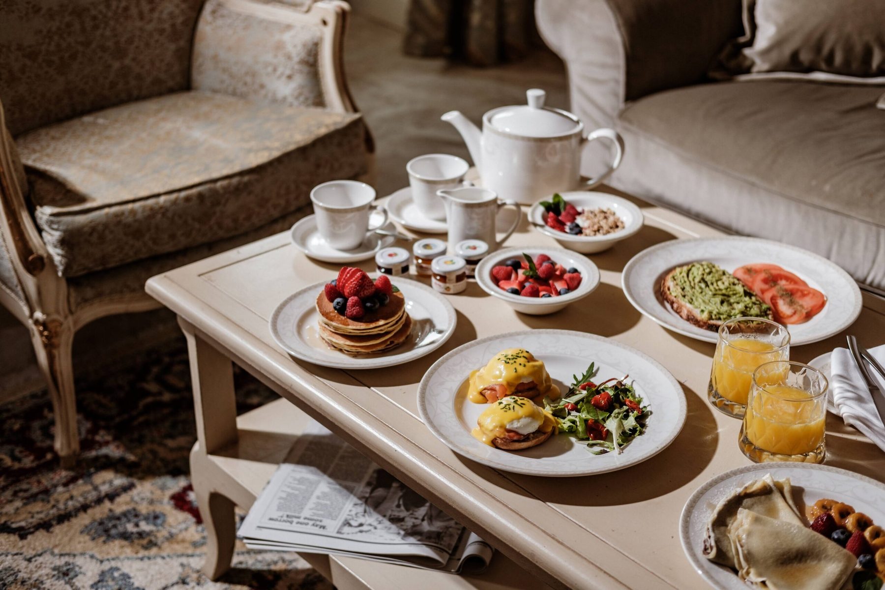 Breakfast dishes and a teapot on a table beside upholstered chairs.