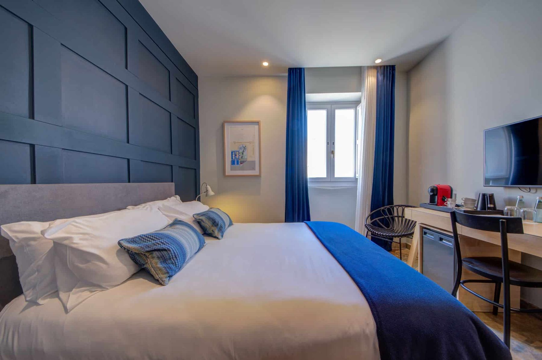 Manoel bedroom with blue panelled wall and desk beside a window.