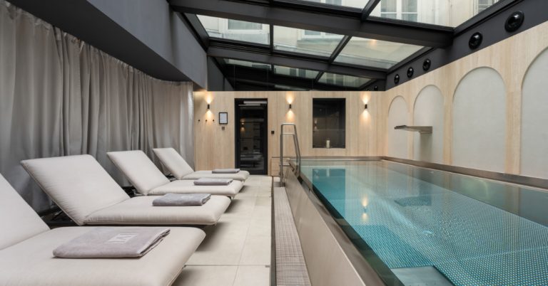 Indoor pool and loungers beneath a glass roof at The Amauris Vienna.