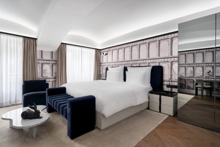 Bed, dark blue chairs and architectural patterned walls in an Amauris Deluxe room.