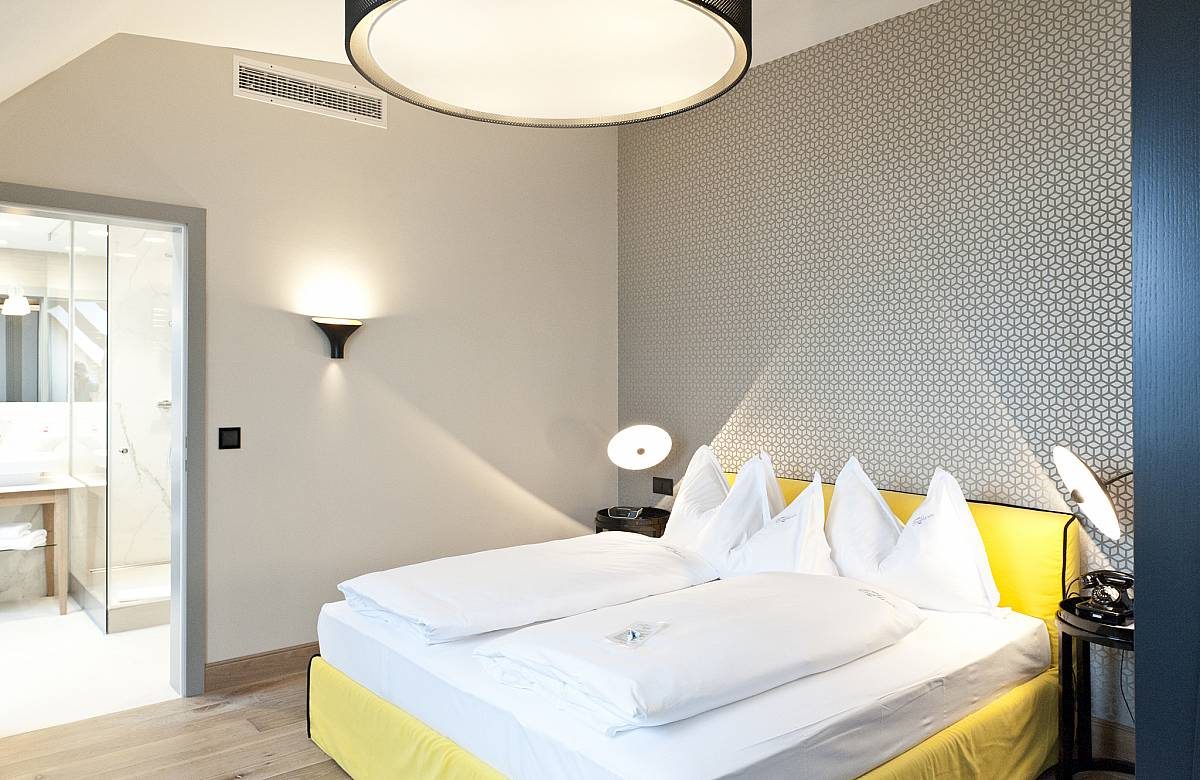 Bed with yellow accent upholstery and a visible doorway into the bathroom at Hotel Beethoven.