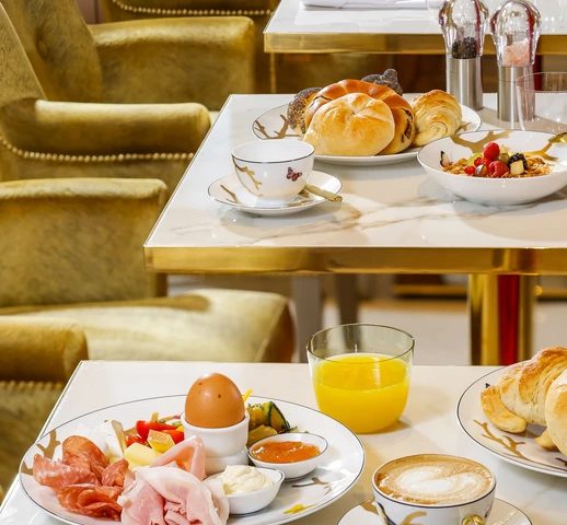 Coffee, pastries, fruit and an egg on a breakfast table beside gold-toned seating.
