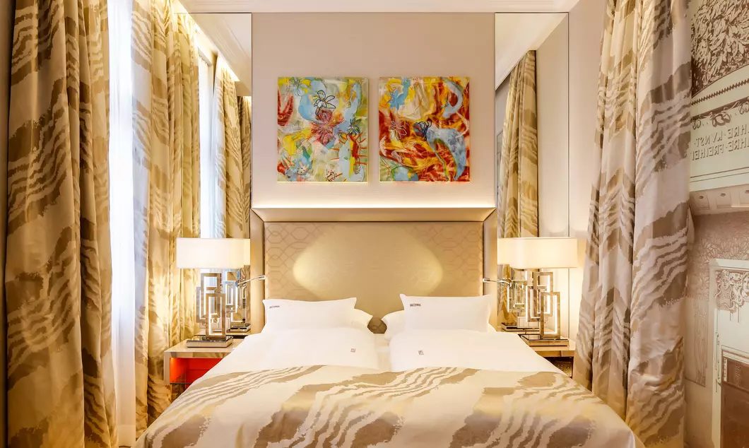 Bed beneath two colourful artworks with patterned curtains at Das Tyrol.