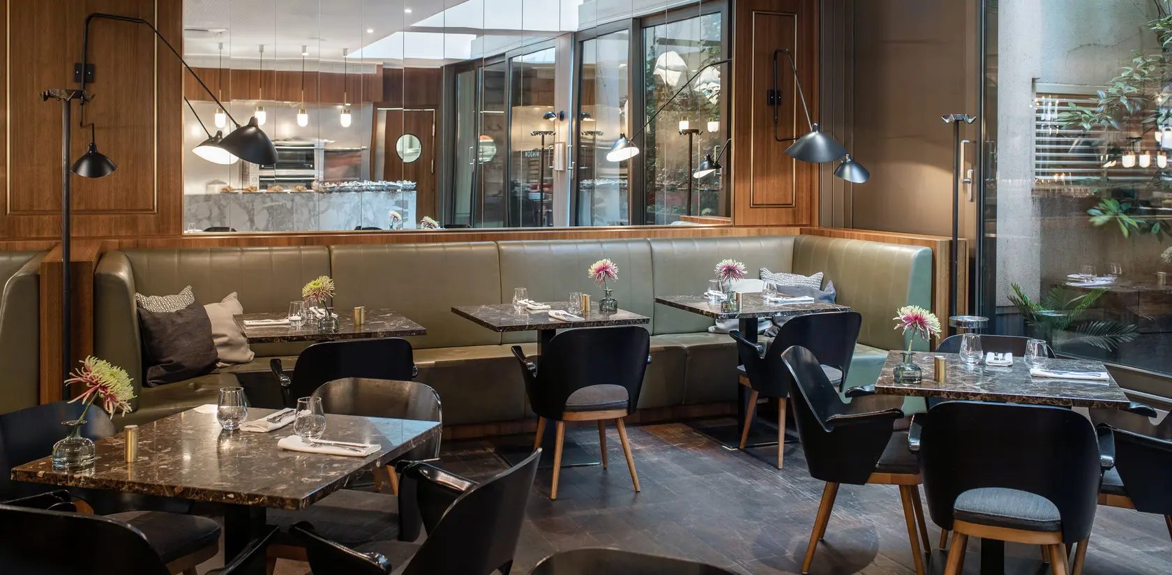 Marble tables, dark chairs and upholstered seating inside The Guesthouse Vienna’s brasserie.