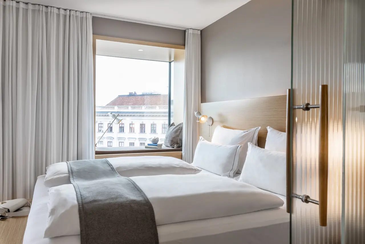 Bed with separate duvets beside a window and grey curtains at The Guesthouse Vienna.