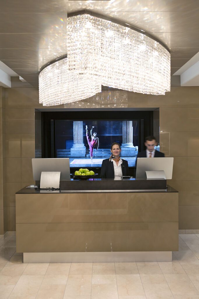 Reception desk beneath a curved chandelier at The Harmonie Vienna.