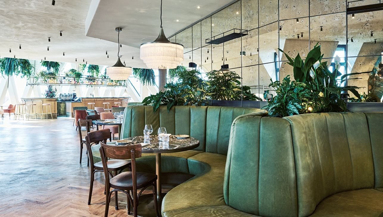 Green upholstered banquettes, plants and hanging lights inside Chez Bernard.