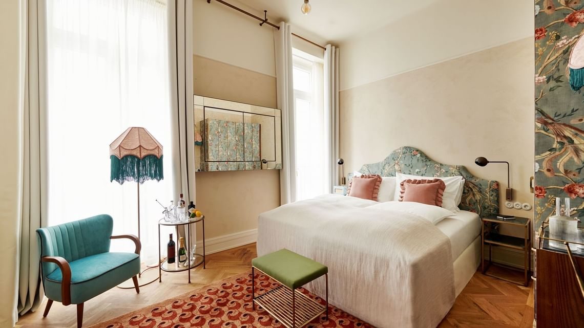 Bed, green chair and patterned rug beside tall windows in a MOTTO DELUXE room.