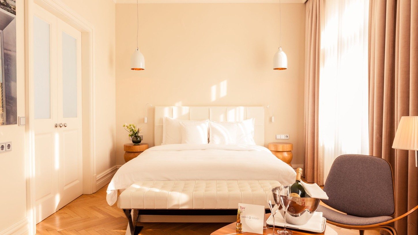 Pale bedroom with a bed, grey armchair and round table at Sans Souci Wien.