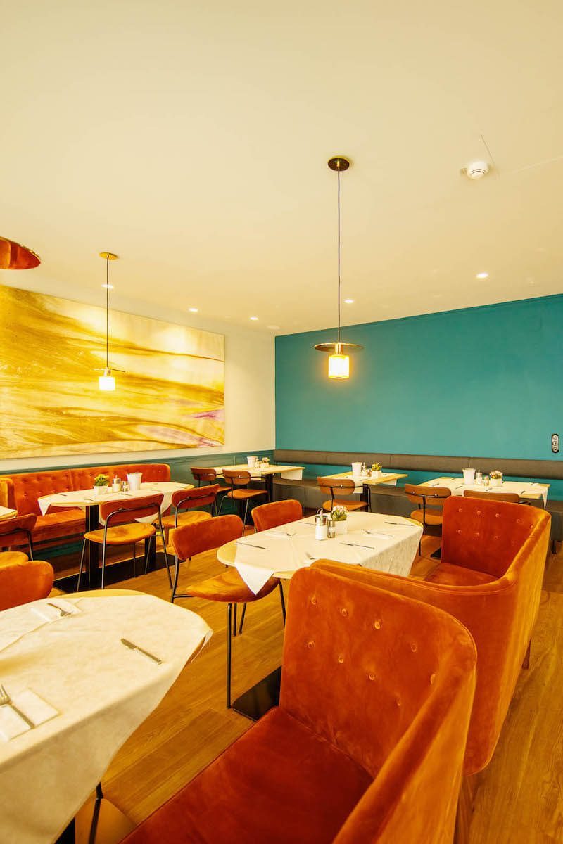 Set dining tables, orange chairs and a large artwork in Der Wilhelmshof’s breakfast room.