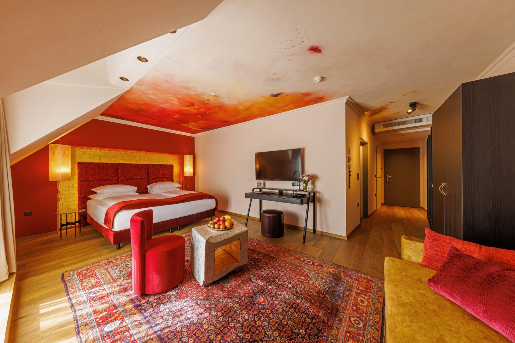 Orange and gold bedroom with painted ceiling, seating and a sofa at Der Wilhelmshof.